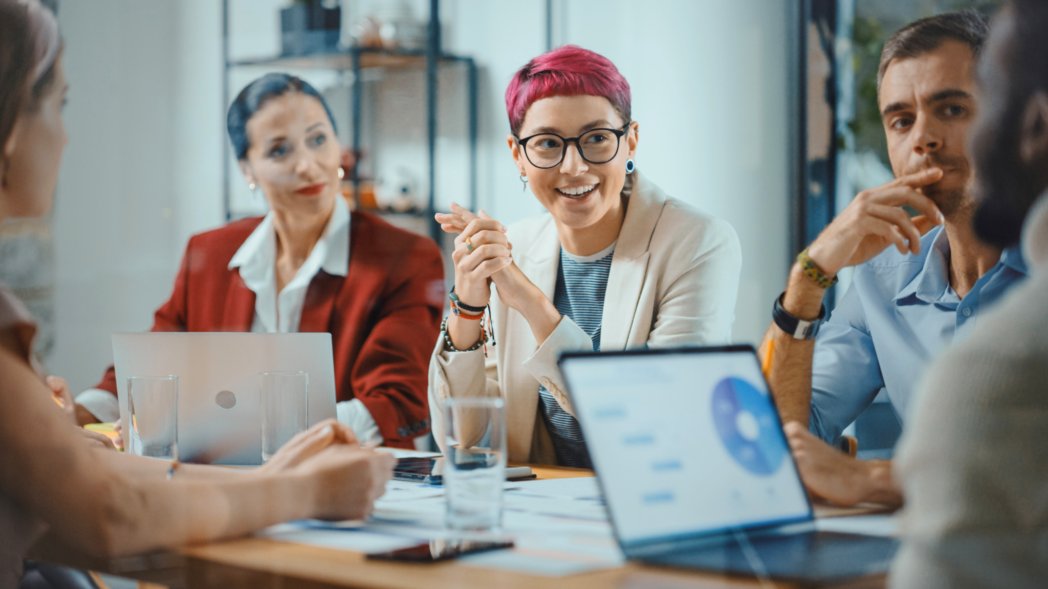 Persönlichkeitsanalyse «INSIGHTS MDI®» - Mitarbeiterin mit pinken Haaren und Brille lächelnd im Gespräch während eines Meetings